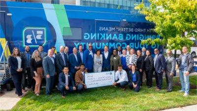 A group of people stand in front of a truck with the Fifth Third Bank logo on it and smile for the camera. Two young men kneel in the middle and hold an oversized check made out to Grand Valley State University.